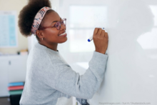 A smiling woman writes on a whiteboard.